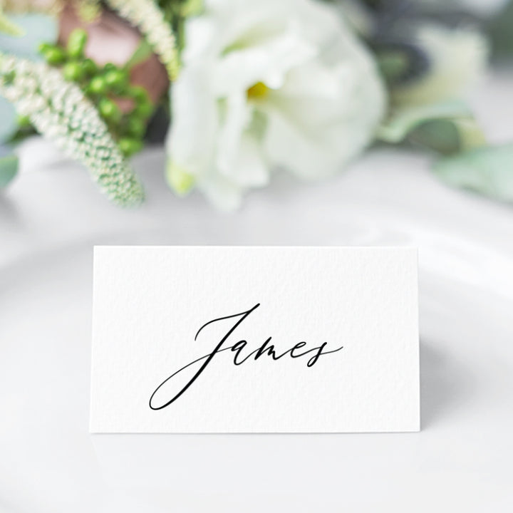 Folded wedding place card with guest name in black calligraphy font and monogram on the back.
