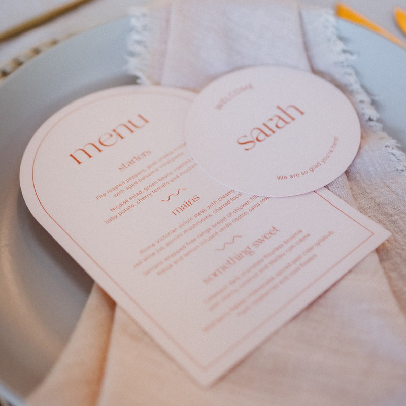 Round wedding place cards with matching arch menu in peach and red. Modern minimal design.