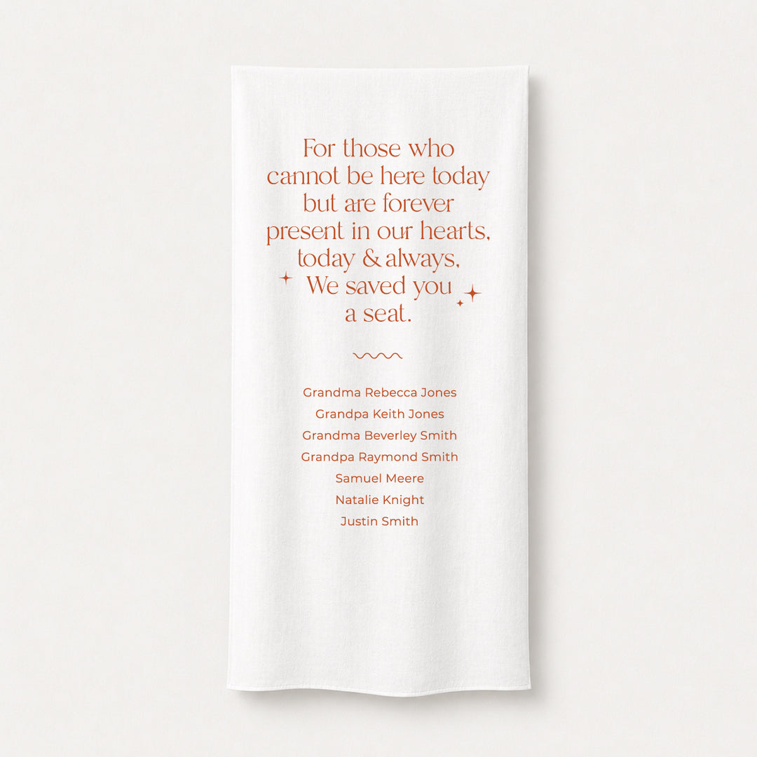 A white fabric memorial printed sign draped over a wooden chair with guest names printed and a poem &