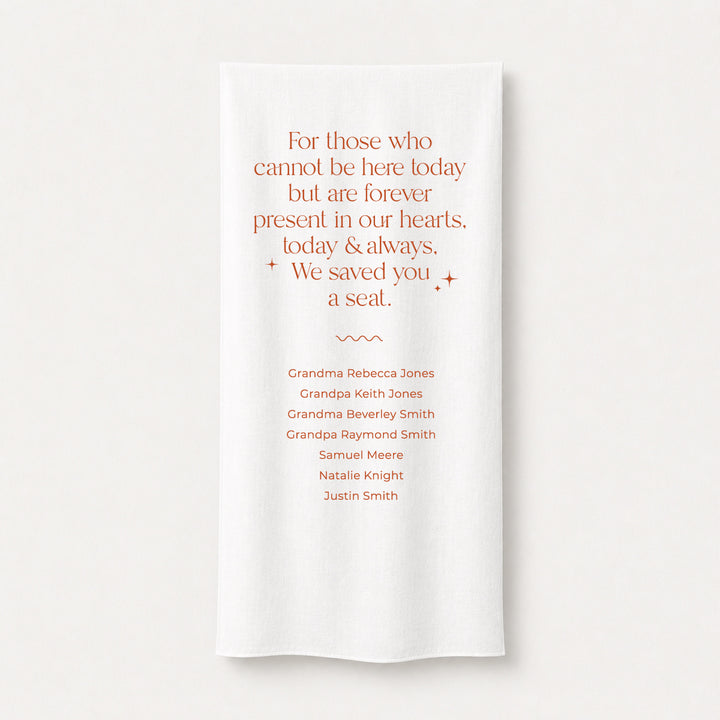A white fabric memorial printed sign draped over a wooden chair with guest names printed and a poem &