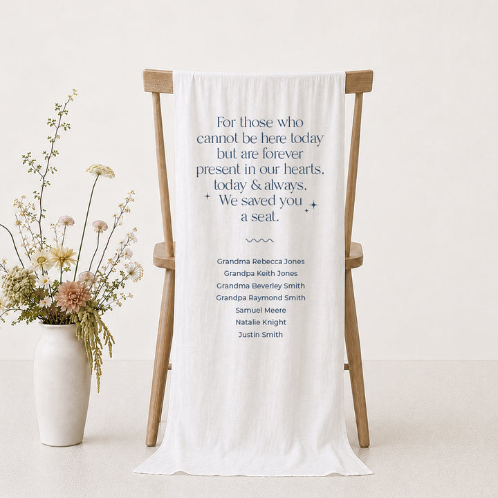 A white fabric memorial printed sign draped over a wooden chair with guest names printed and a poem &