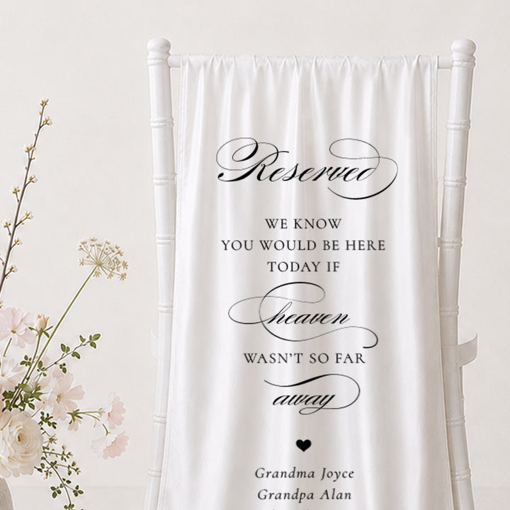 A close up of a white fabric memorial banner draped over a white wedding chair, printed with elegant black script and serif text in Australia honouring loved ones.