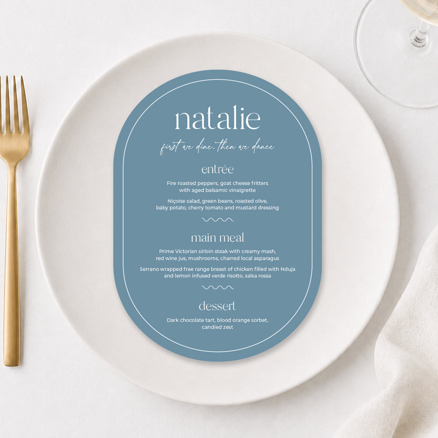Dusty blue arch wedding menu with white typography styled on a white dinner plate