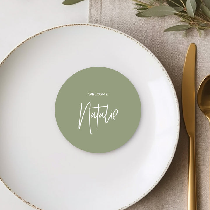 Round wedding place cards or escort cards, white ink on green card with Welcome and guest names.