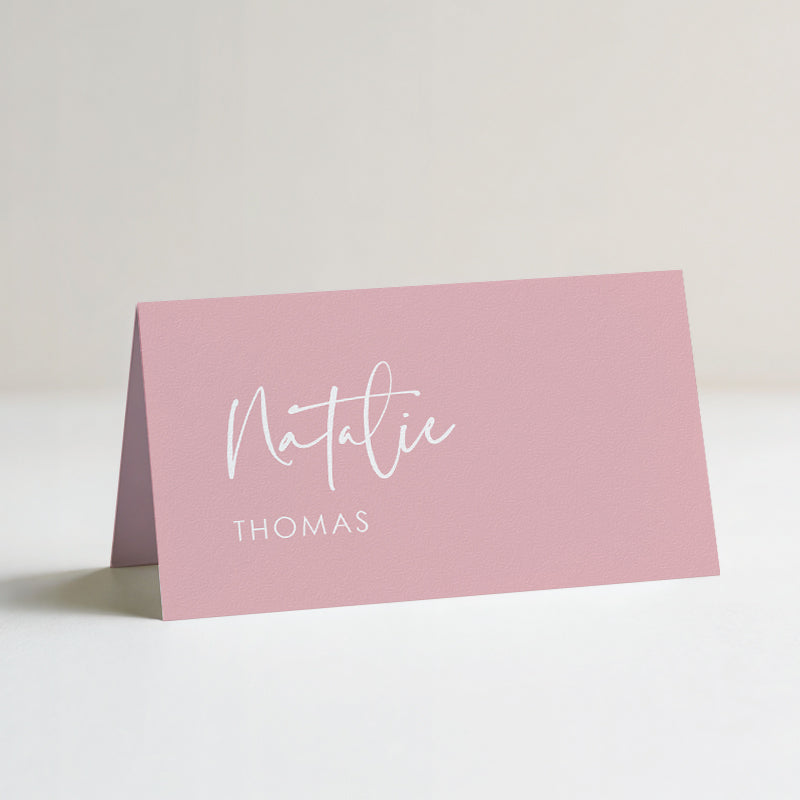 A pink personalised wedding folded tent place card with white text.