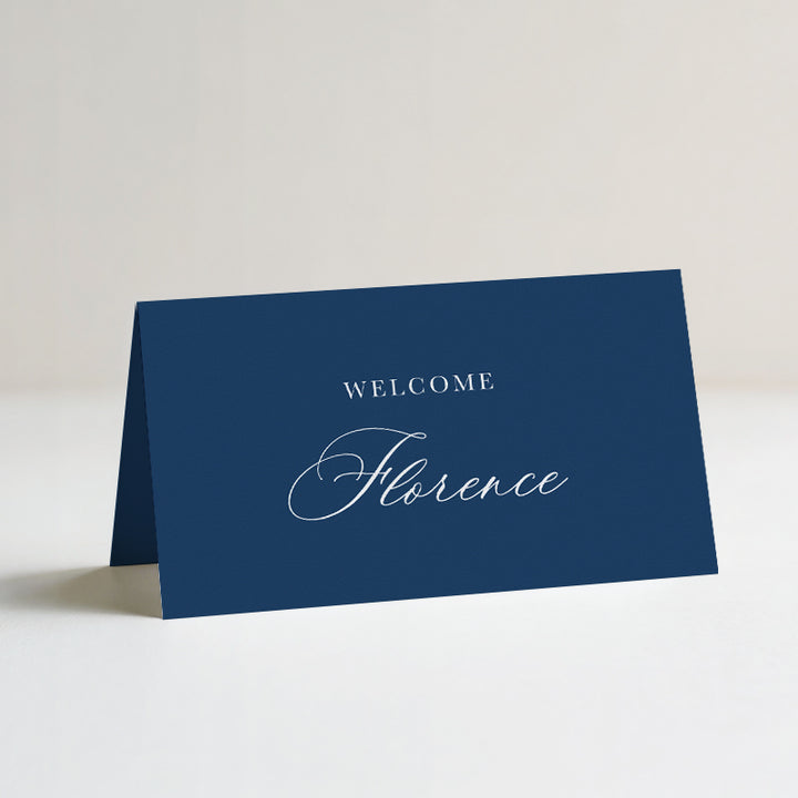 A navy blue folded wedding place card with the words &