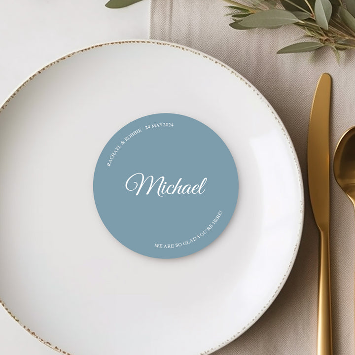 Round wedding place cards or name cards on blue cardstock with white ink. Calligraphy font with we are so glad you're here.