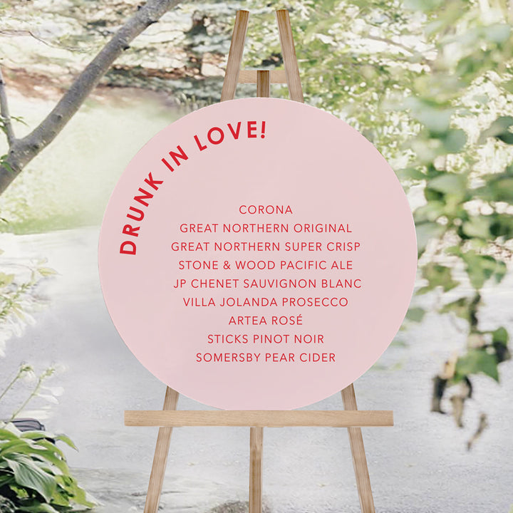 Round wedding bar sign printed on foamboard in pink and hot pink or red. Drunk in love heading.