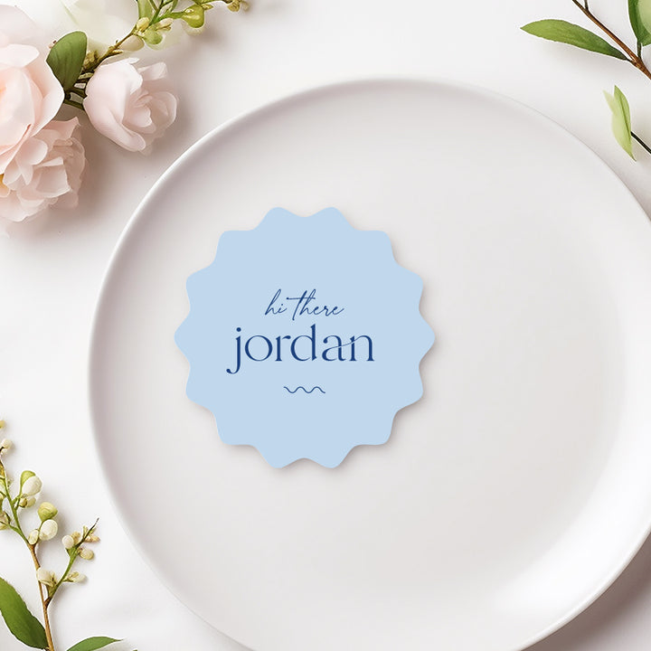 Wavy round wedding place cards with hi there and guest names in blue on light blue.