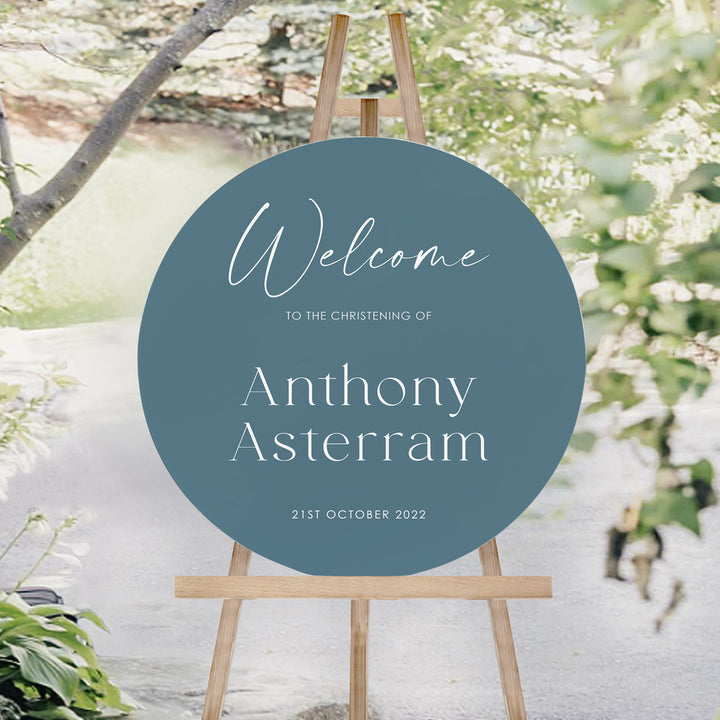 Round Baptism or Christening welcome sign for boys in teal blue with white text. Christening welcome sign on an easel. Peach Perfect.