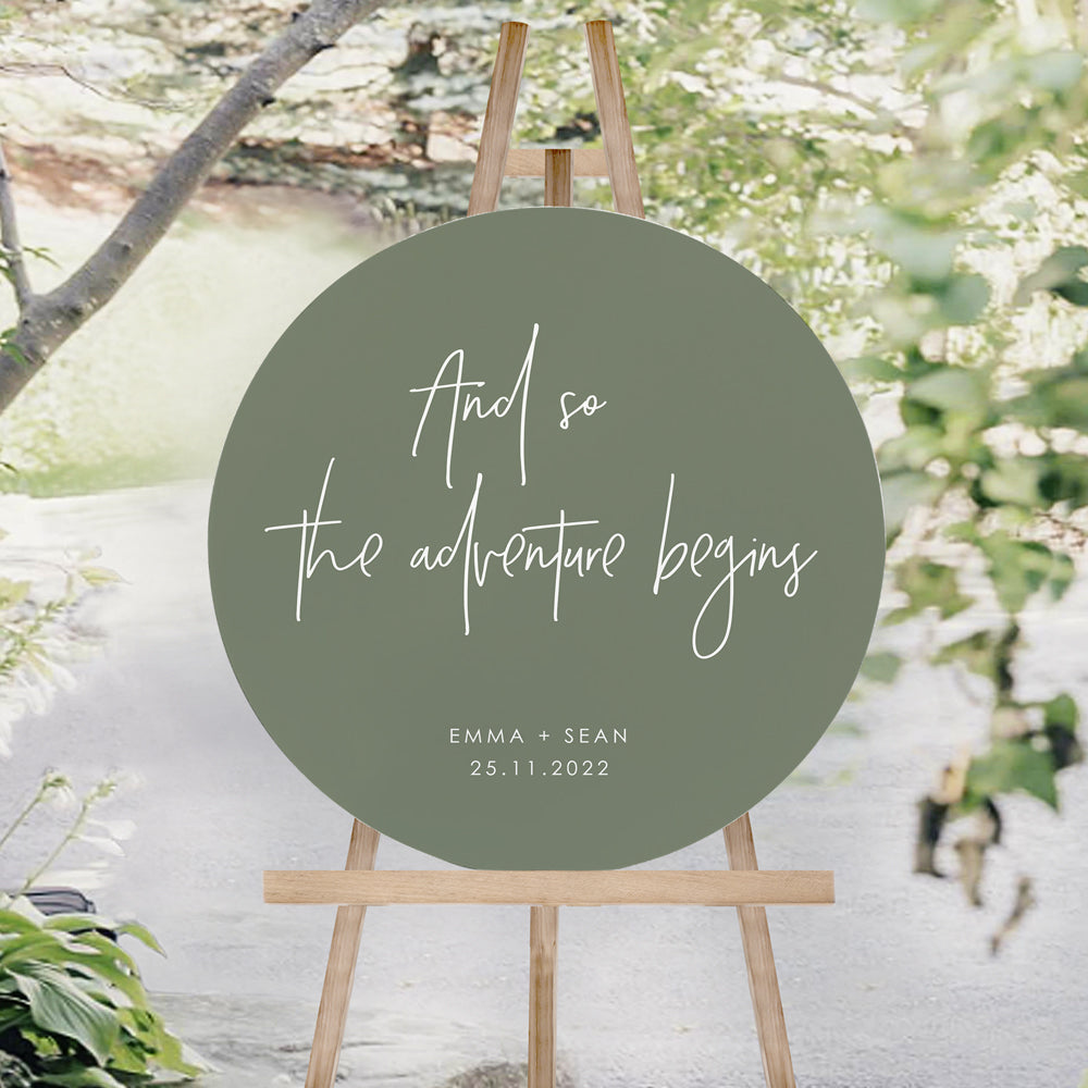 And so the adventure begins wedding welcome sign. Soft green neutral circle foamboard sign with white text.