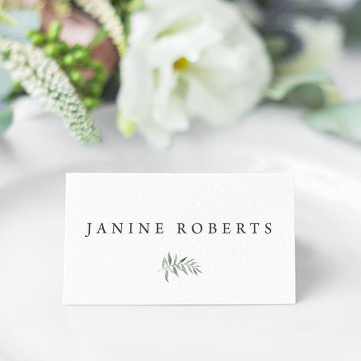 Wedding place card folded and featuring a soft green watercolour leaf and your guest names in natural charcoal.
