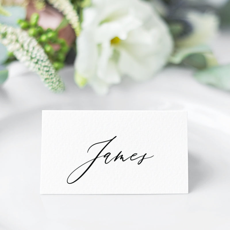 Folded wedding place card with guest name in black calligraphy font and monogram on the back.