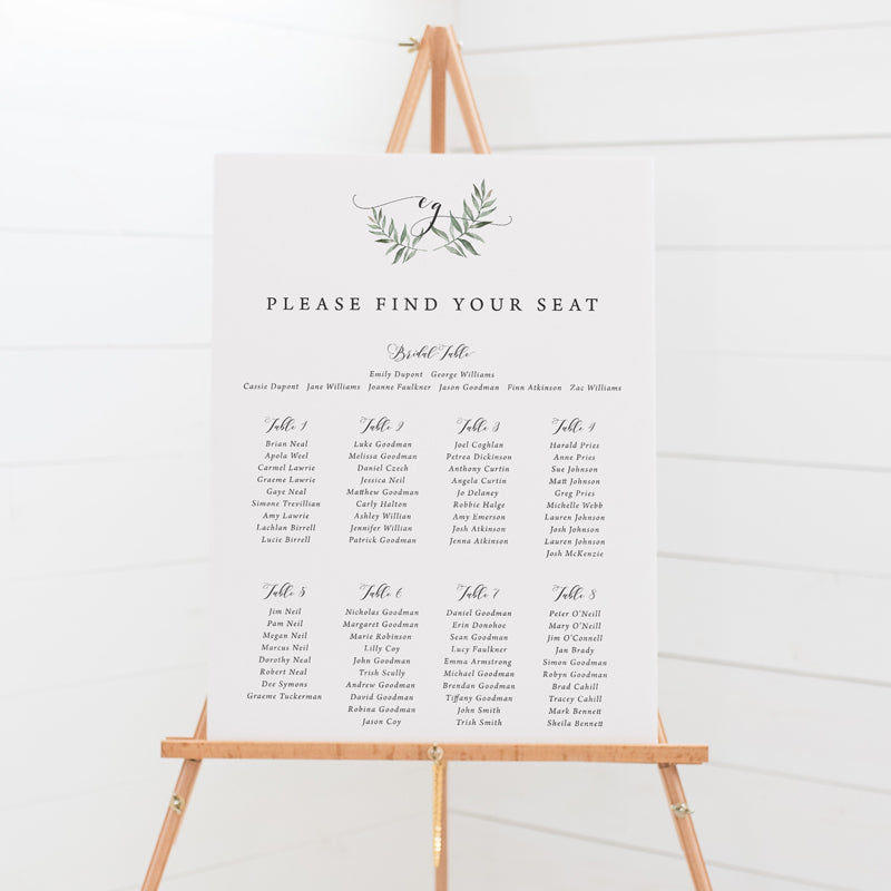 Wedding seating chart with monogram of bride and grooms initials in calligraphy and leafy wreath. 