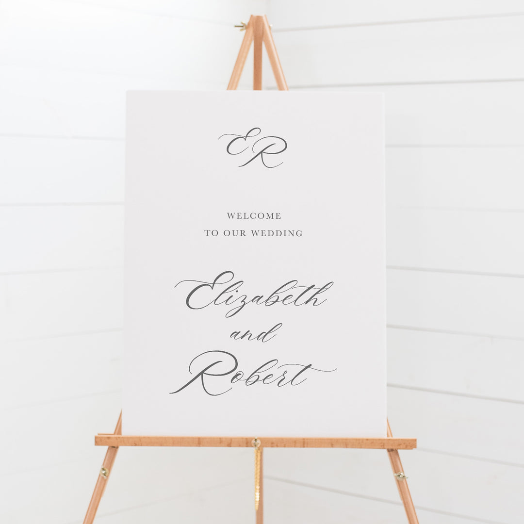 Traditional wedding welcome sign on board with calligraphy for the bride and grooms name and monogram at top.